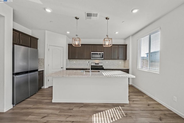 kitchen with sink, light hardwood / wood-style floors, stainless steel appliances, dark brown cabinets, and a center island with sink