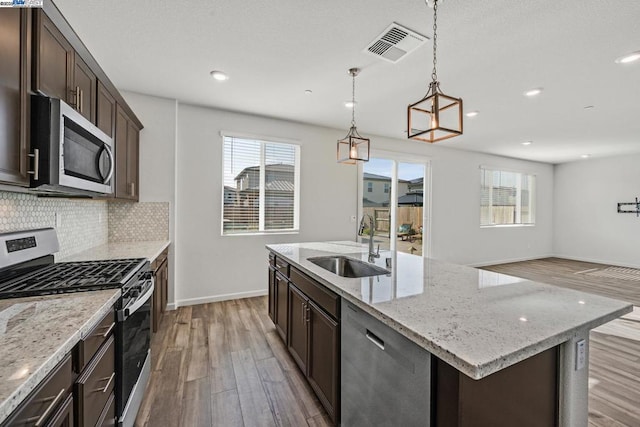 kitchen with pendant lighting, sink, stainless steel appliances, light stone countertops, and an island with sink