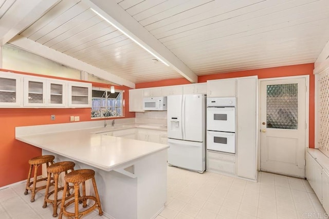 kitchen featuring a peninsula, white appliances, white cabinets, light floors, and a kitchen bar