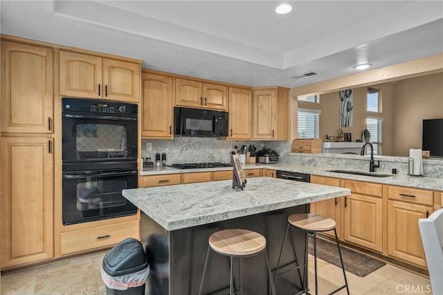 kitchen featuring sink, a breakfast bar area, black appliances, a kitchen island, and a raised ceiling