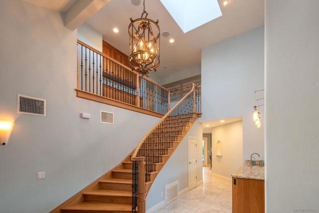 stairway featuring a towering ceiling, a notable chandelier, and a skylight