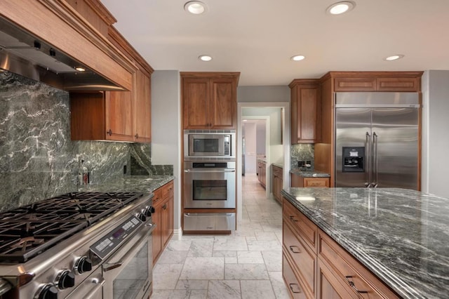 kitchen with built in appliances, decorative backsplash, custom range hood, and dark stone counters