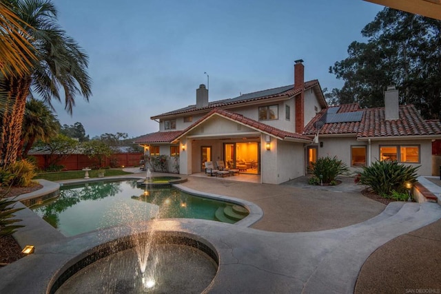 back house at dusk with a pool with hot tub, a patio, and solar panels