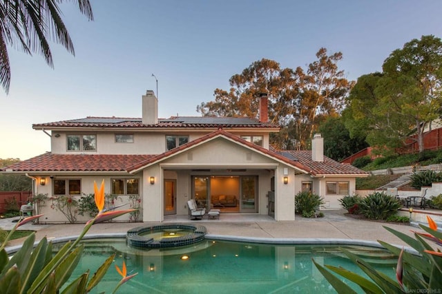 back house at dusk featuring a pool with hot tub, a patio area, and solar panels