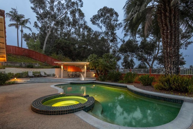 pool at dusk featuring an in ground hot tub and a patio