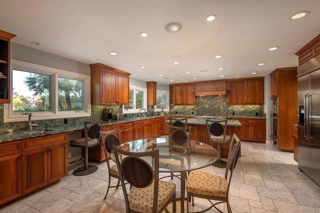 kitchen with appliances with stainless steel finishes, a kitchen island, a kitchen bar, decorative backsplash, and dark stone counters