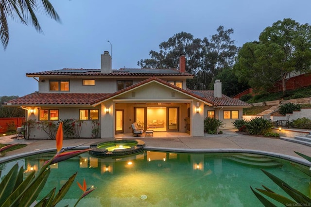 back house at dusk with a swimming pool with hot tub, a patio, and solar panels