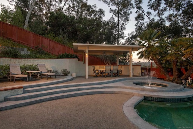 pool at dusk with an in ground hot tub, pool water feature, and a patio