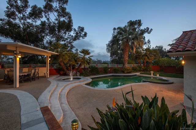 pool at dusk with a patio and an in ground hot tub