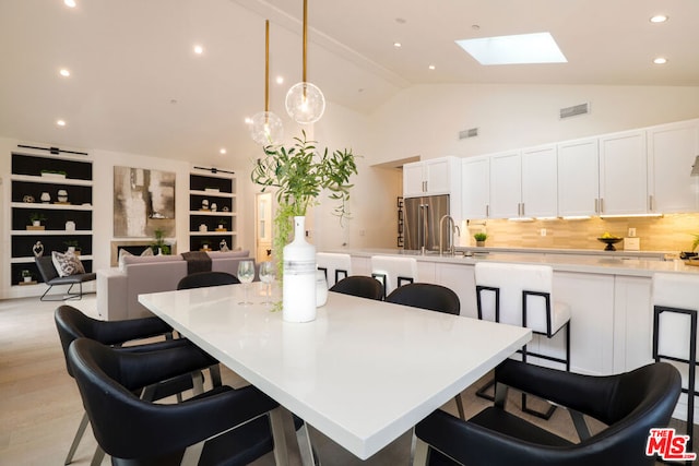 dining space featuring a skylight, sink, high vaulted ceiling, and light hardwood / wood-style flooring