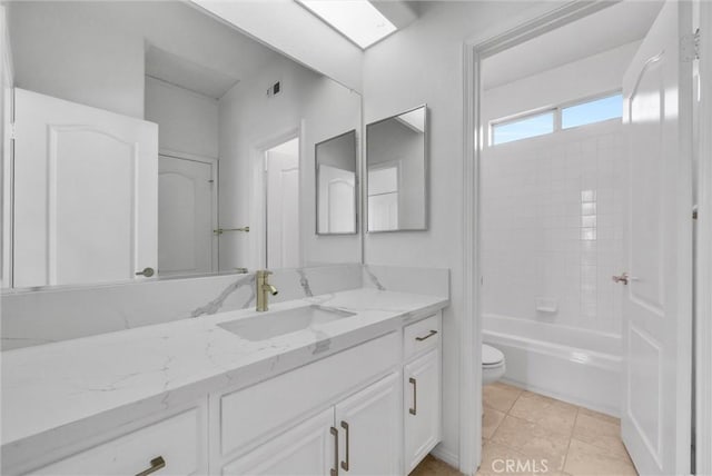 full bathroom with tiled shower / bath, a skylight, tile patterned flooring, vanity, and toilet