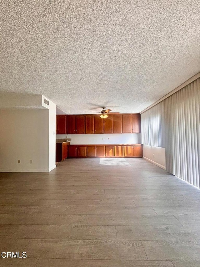 unfurnished living room featuring ceiling fan, light hardwood / wood-style flooring, and a textured ceiling