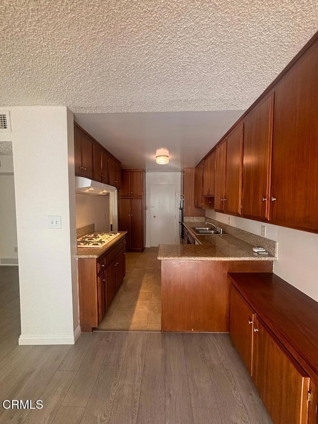 kitchen featuring white gas stovetop, kitchen peninsula, sink, and light hardwood / wood-style flooring