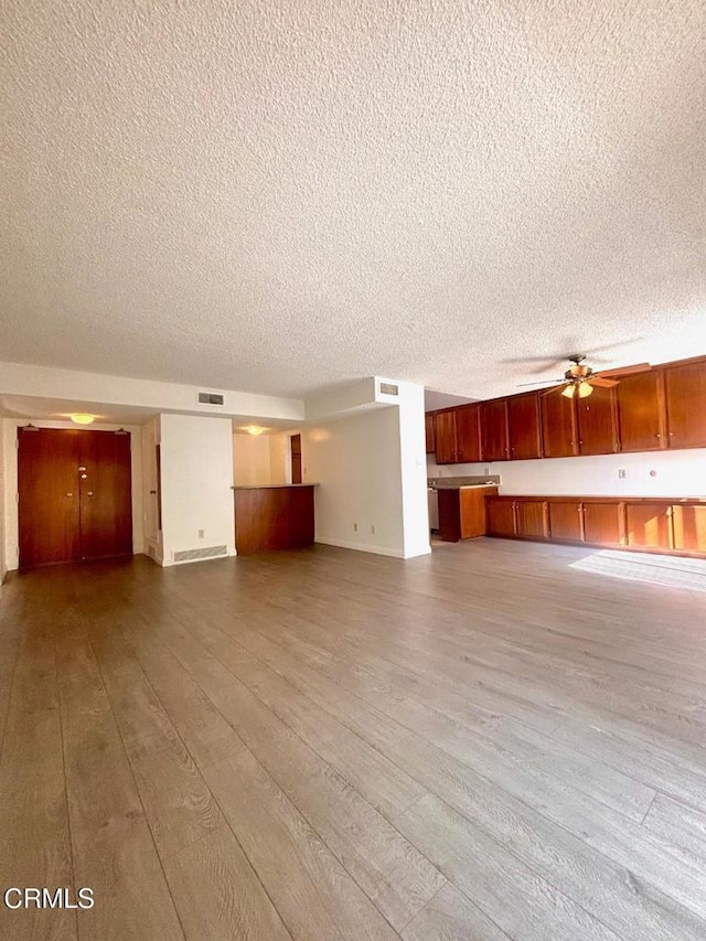 unfurnished living room with a textured ceiling, ceiling fan, and light hardwood / wood-style flooring