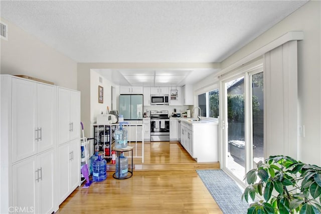 kitchen featuring appliances with stainless steel finishes, sink, white cabinets, and light hardwood / wood-style floors