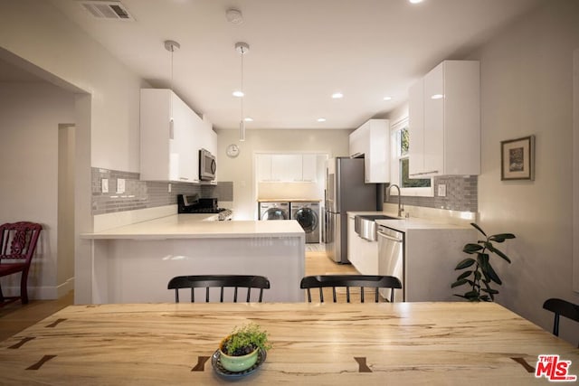 kitchen featuring white cabinetry, appliances with stainless steel finishes, independent washer and dryer, and decorative light fixtures