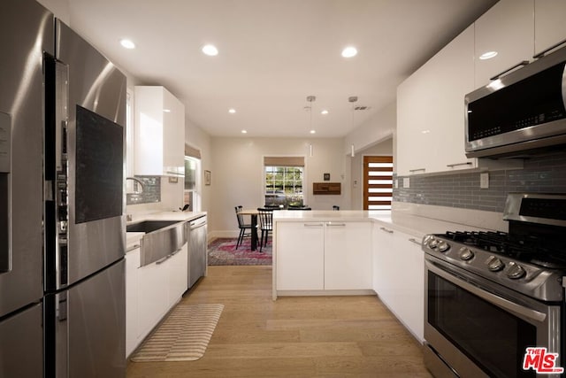 kitchen with white cabinetry, decorative light fixtures, kitchen peninsula, and appliances with stainless steel finishes