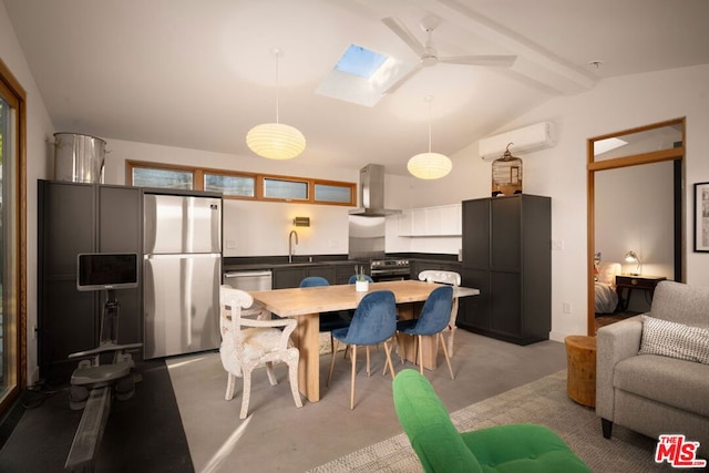 kitchen with vaulted ceiling with skylight, decorative light fixtures, a wall mounted AC, stainless steel appliances, and wall chimney exhaust hood