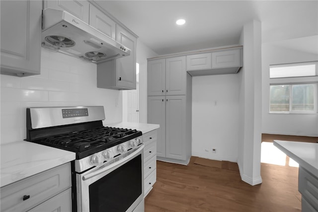 kitchen with stainless steel gas stove, ventilation hood, tasteful backsplash, light stone countertops, and dark wood-type flooring