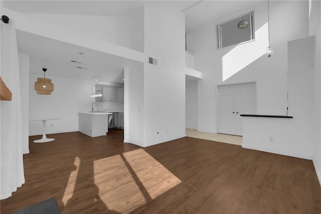 unfurnished living room with wood-type flooring, sink, and a high ceiling