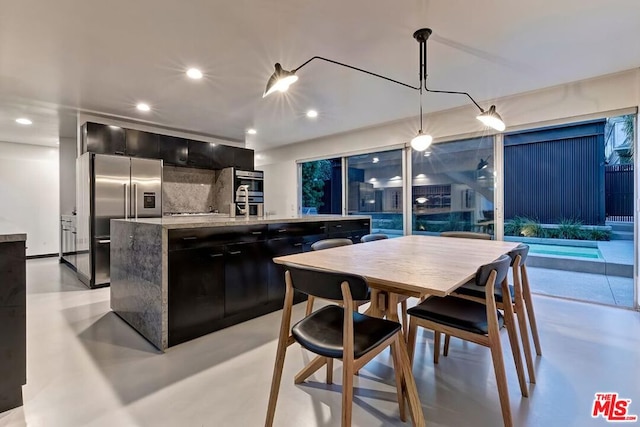 kitchen with tasteful backsplash, appliances with stainless steel finishes, a kitchen island with sink, and hanging light fixtures