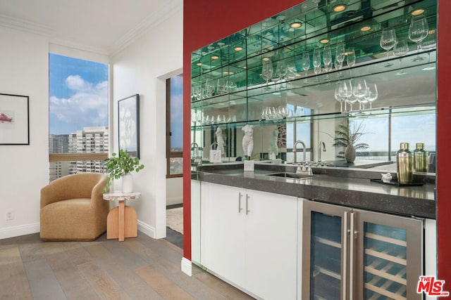 bar featuring sink, hardwood / wood-style flooring, wine cooler, a wealth of natural light, and ornamental molding