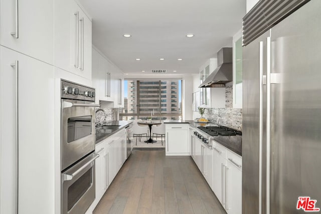 kitchen with dark hardwood / wood-style floors, sink, white cabinets, stainless steel appliances, and wall chimney exhaust hood