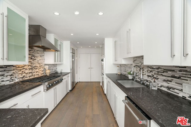 kitchen with stainless steel appliances, white cabinetry, sink, and wall chimney range hood