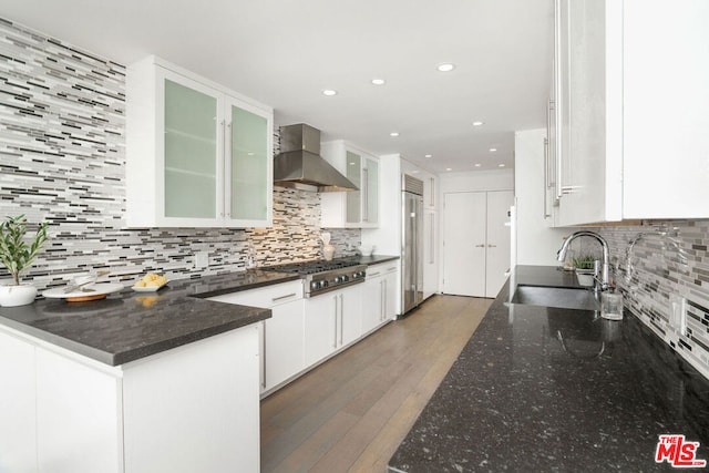 kitchen featuring wall chimney range hood, sink, dark wood-type flooring, stainless steel appliances, and white cabinets