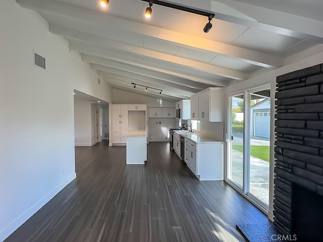 kitchen featuring dark wood-type flooring, rail lighting, sink, vaulted ceiling with beams, and white cabinets