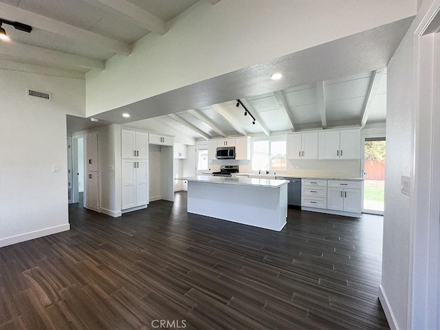 kitchen featuring dark wood-type flooring, vaulted ceiling with beams, appliances with stainless steel finishes, and white cabinets