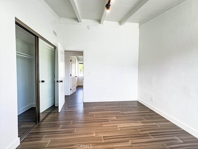 unfurnished bedroom featuring beamed ceiling, dark hardwood / wood-style floors, and a closet