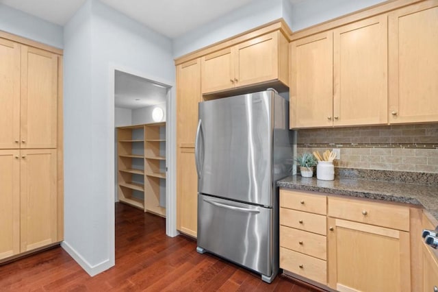 kitchen with dark wood-type flooring, stainless steel refrigerator, dark stone countertops, decorative backsplash, and light brown cabinets