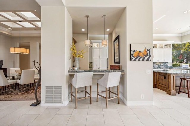 kitchen with dark stone countertops, decorative light fixtures, a breakfast bar, and white cabinets