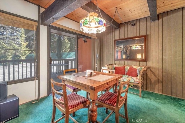 dining room with wood ceiling, beam ceiling, dark carpet, and wood walls