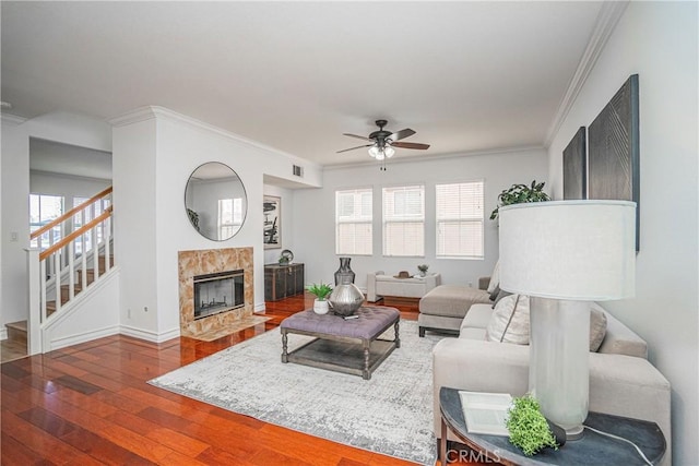 living room featuring a tiled fireplace, hardwood / wood-style flooring, ornamental molding, and ceiling fan