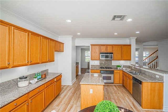 kitchen featuring sink, light stone counters, light hardwood / wood-style flooring, appliances with stainless steel finishes, and a kitchen island