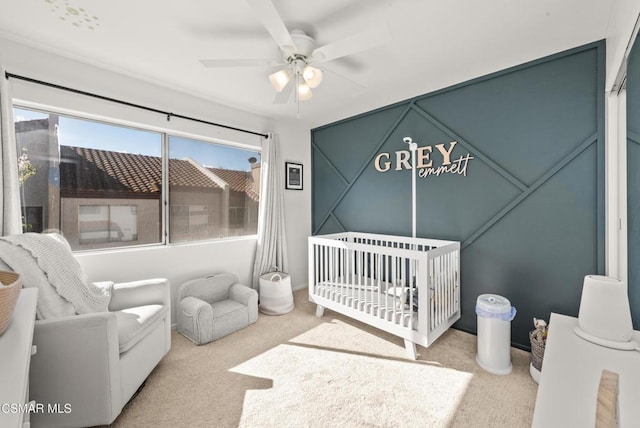 carpeted bedroom featuring ceiling fan and a crib