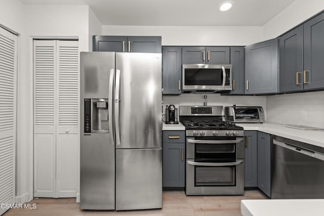 kitchen with tasteful backsplash, appliances with stainless steel finishes, gray cabinetry, and light hardwood / wood-style flooring