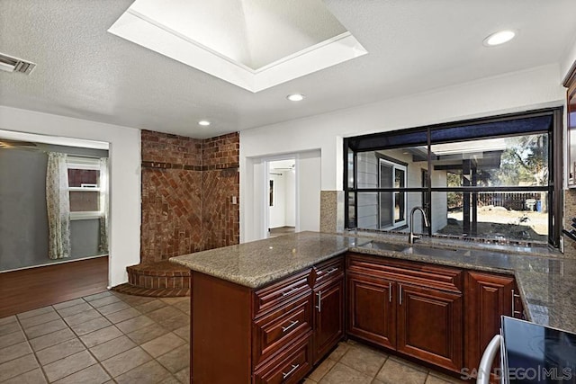 kitchen featuring sink, a textured ceiling, dark stone countertops, range with electric stovetop, and kitchen peninsula