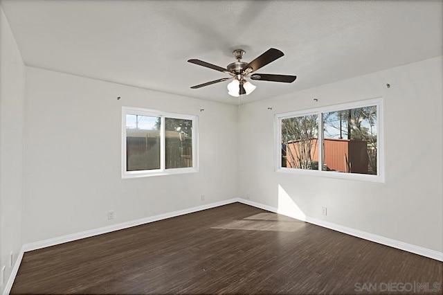 spare room featuring dark wood-type flooring, ceiling fan, and plenty of natural light