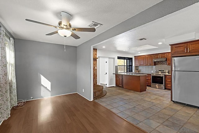 kitchen with light wood-type flooring, decorative backsplash, ceiling fan, stainless steel appliances, and a textured ceiling