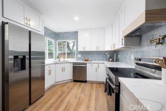 kitchen featuring tasteful backsplash, white cabinets, light stone counters, stainless steel appliances, and custom range hood