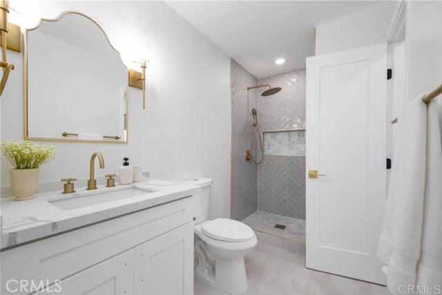 bathroom with a tile shower, vanity, and toilet