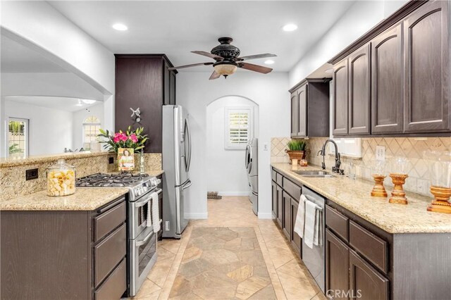 kitchen with sink, appliances with stainless steel finishes, dark brown cabinets, tasteful backsplash, and light stone countertops