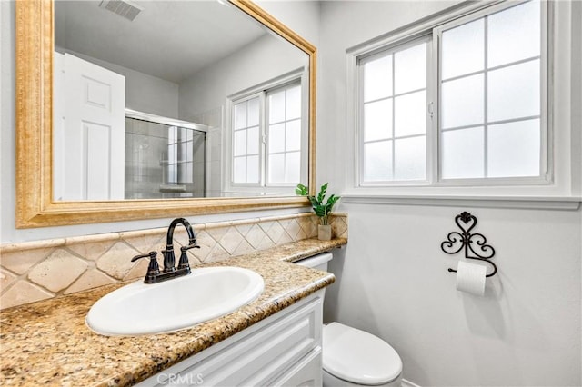 bathroom featuring tasteful backsplash, vanity, a shower with door, and toilet