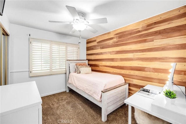 unfurnished bedroom with ceiling fan, dark carpet, wooden walls, and a closet