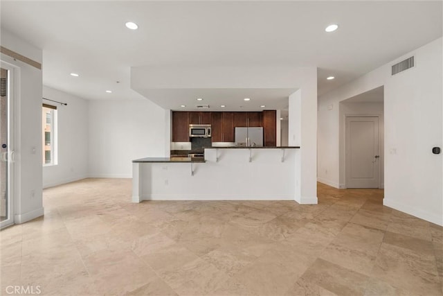 kitchen with fridge with ice dispenser, dark brown cabinetry, a breakfast bar, and kitchen peninsula