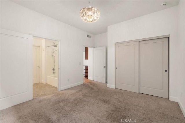 unfurnished bedroom with a notable chandelier, ensuite bath, light colored carpet, and a closet