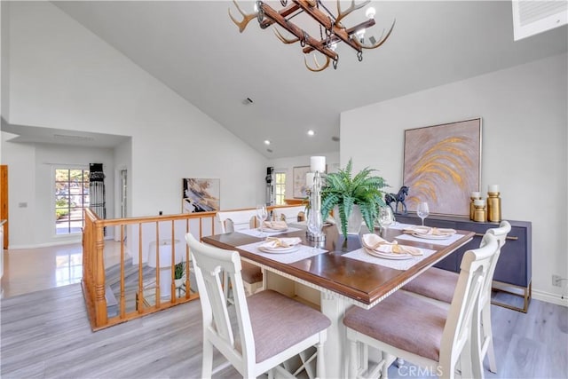 dining space featuring high vaulted ceiling, a healthy amount of sunlight, a chandelier, and light hardwood / wood-style floors